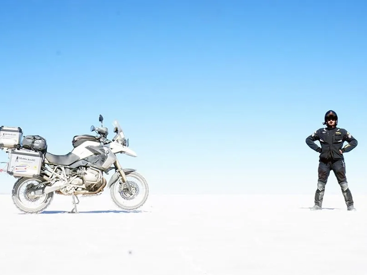 Motociclista de pie junto a su moto en un paisaje desértico y despejado.