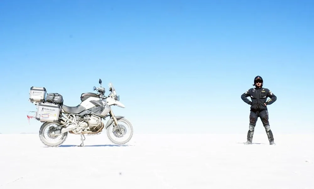 Motociclista de pie junto a su moto en un paisaje desértico y despejado.