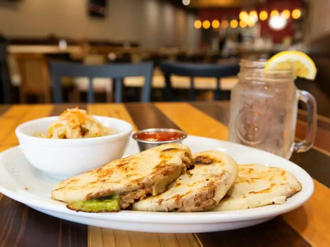 Plato de pupusas con ensalada y bebida en un restaurante.