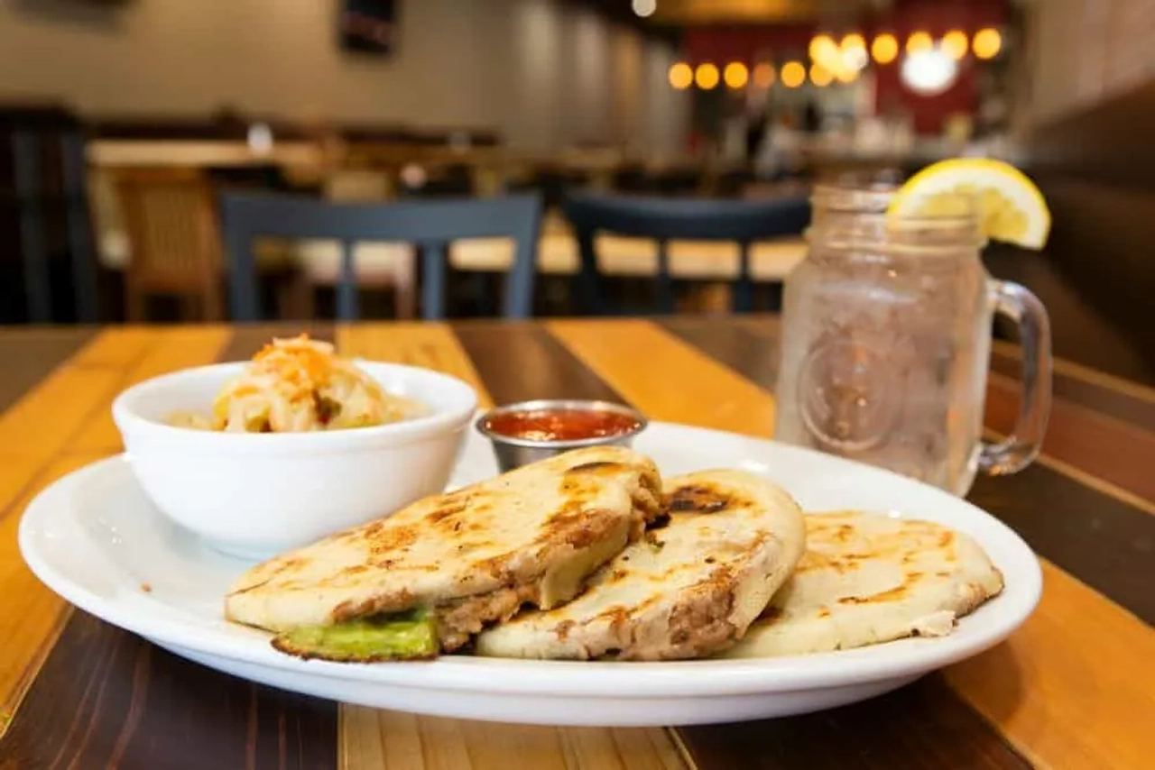 Plato de pupusas con ensalada y bebida en un restaurante.