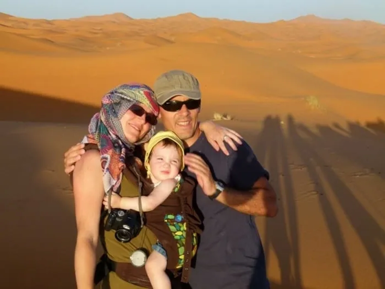 Familia sonriente en el desierto, con un niño pequeño y paisajes de arena.