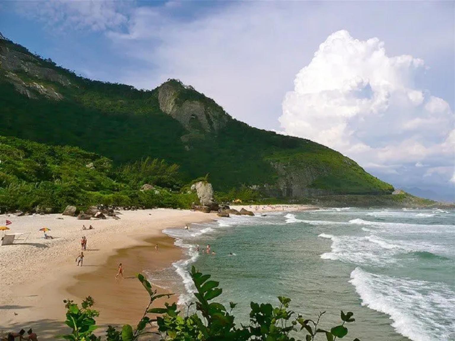Playa con arena, olas y montañas verdes al fondo, ideal para disfrutar.