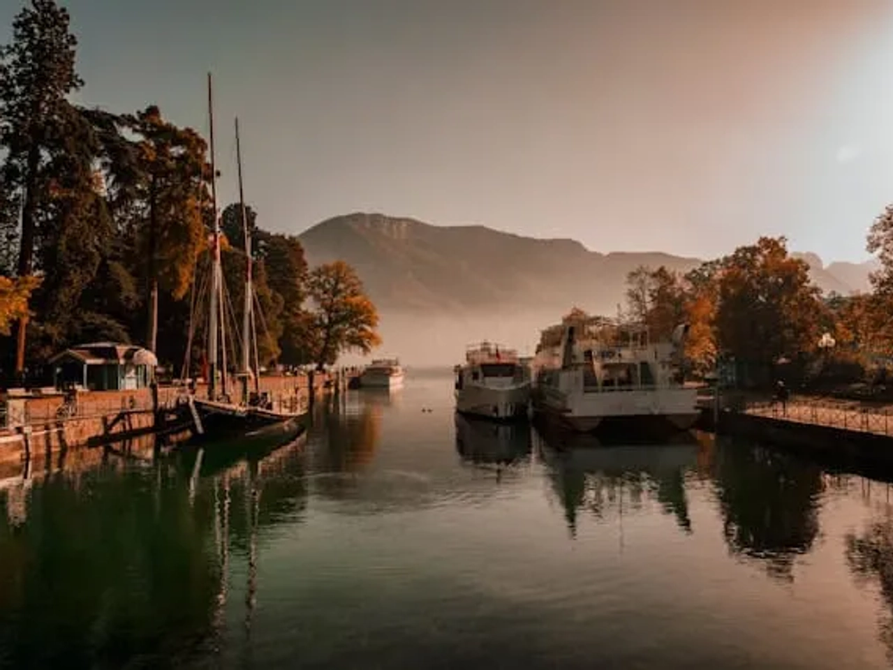 lago ao por do sol com arvores com folhas cor de outono e barcos no rio em Annecy na França