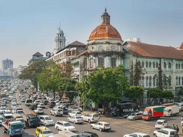 muitos carros numa estrada junto a um edificio grande com cupulas no telhado em Yangon, Myanmar no sudeste asiatico