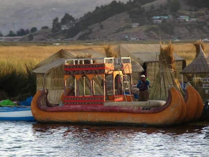 Bote de totora en un lago, con casas de juncos al fondo.