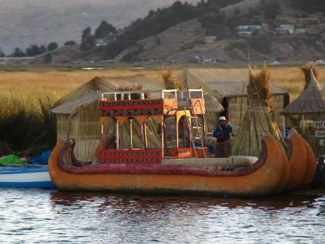 Bote de totora en un lago, con casas de juncos al fondo.