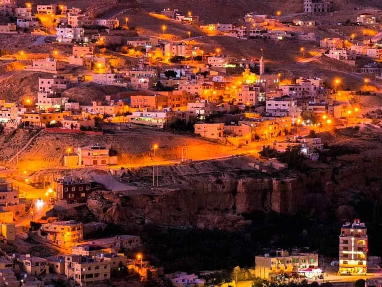 Vista nocturna de una ciudad en Jordania, iluminada por luces cálidas.