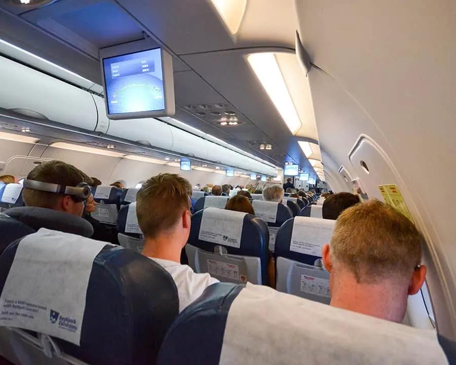 Pasajeros en un avión, con pantallas de entretenimiento y asientos ocupados.