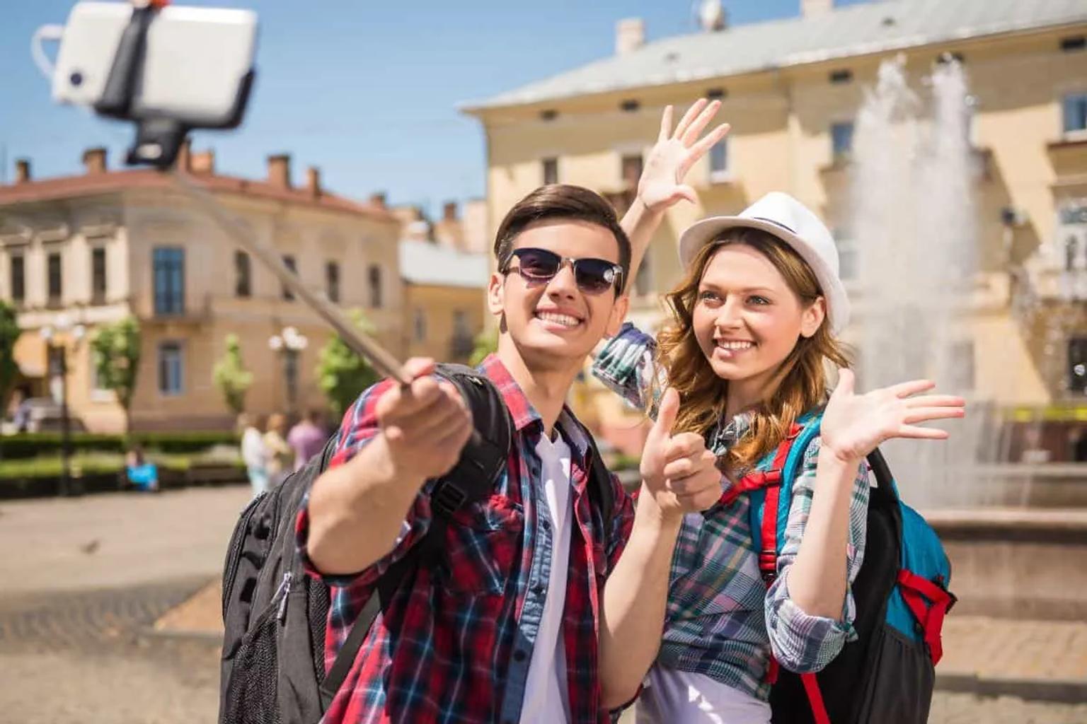 Pareja sonriente tomando una selfie frente a una fuente en un lugar turístico.