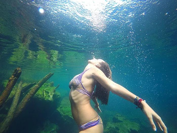 Mujer nadando bajo el agua, rodeada de luz y elementos naturales.