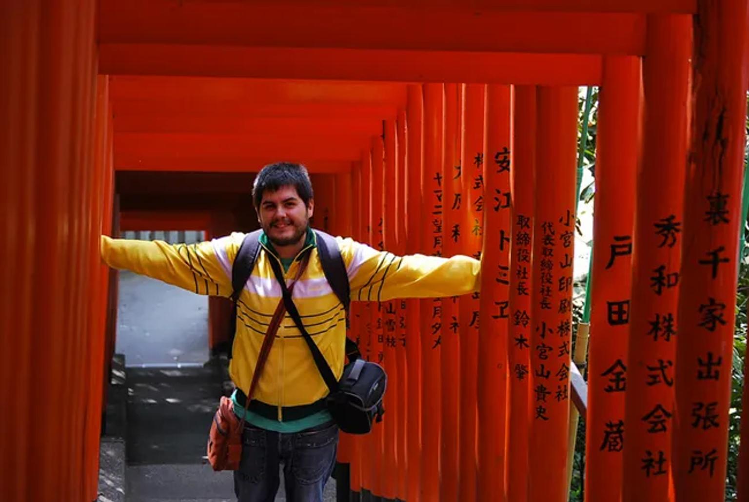 Hombre sonriente en un camino de torii naranjas en Japón.