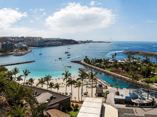vista aerea de barcos, plameiras, casas e pessoas junto à praia de agua azul turquesa em gran canaria nas ilhas canarias
