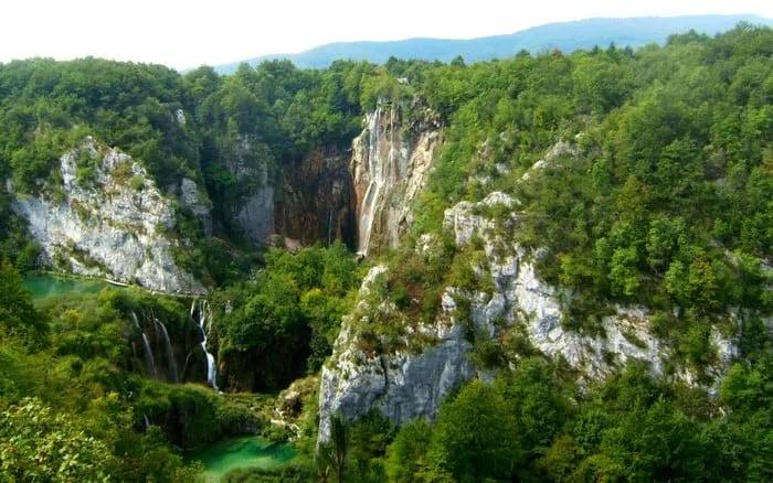 Vista panorámica de un paisaje montañoso con cascadas y lagos rodeados de vegetación.