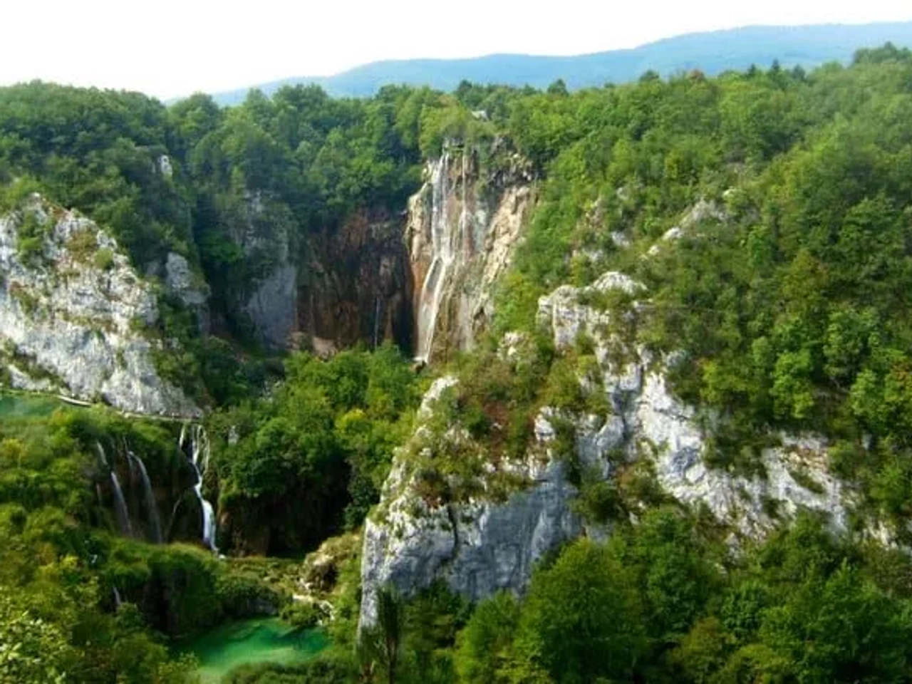 Vista panorámica de un paisaje montañoso con cascadas y lagos rodeados de vegetación.