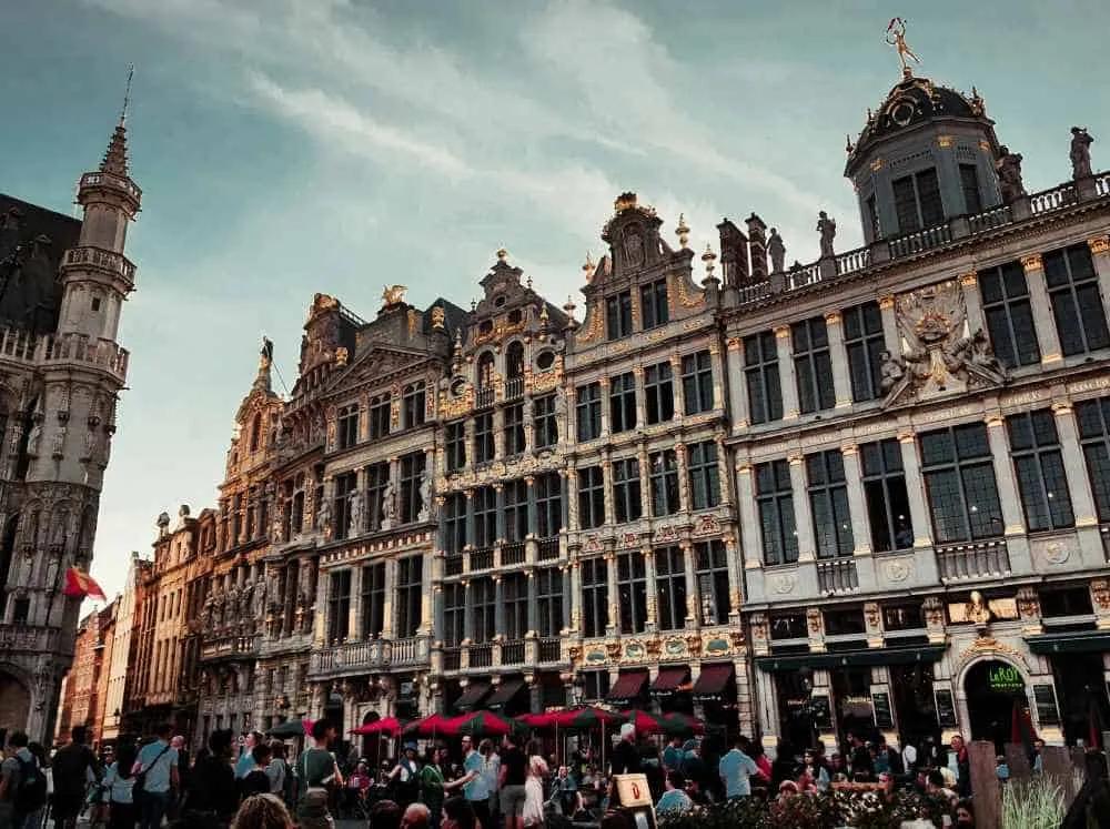 Plaza con edificios históricos y gente disfrutando en Bruselas al atardecer.