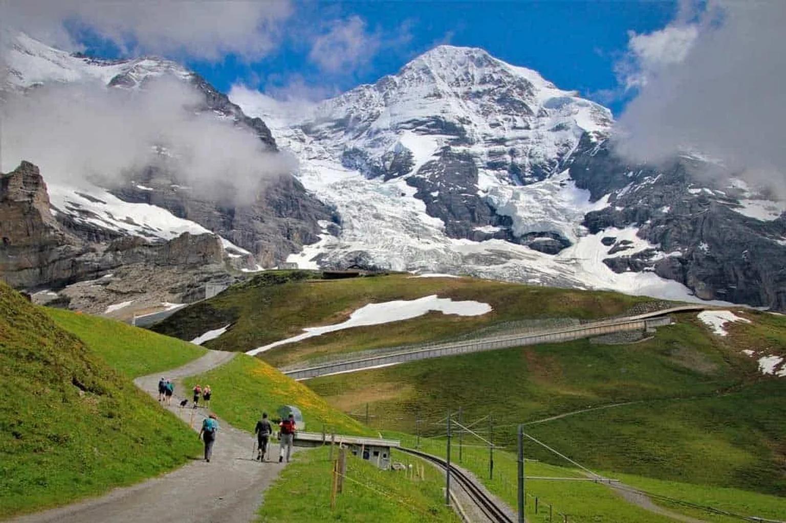 Senderistas en un paisaje montañoso suizo con nieve y nubes.