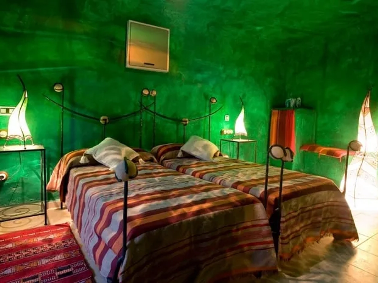 Habitación de hotel con paredes verdes, camas individuales y decoración original.