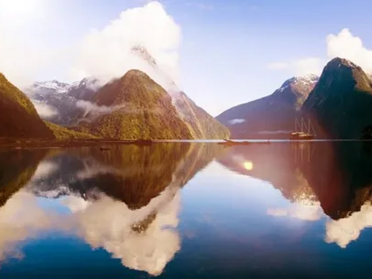 Paisaje montañoso con reflejos en el agua y un barco en la distancia.