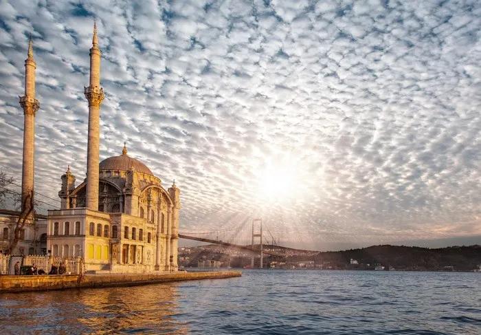 Mezquita junto al agua con un puente y cielo nublado al atardecer.