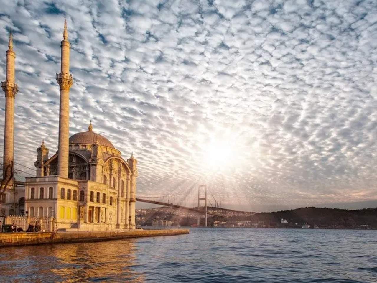 Mezquita junto al agua con un puente y cielo nublado al atardecer.