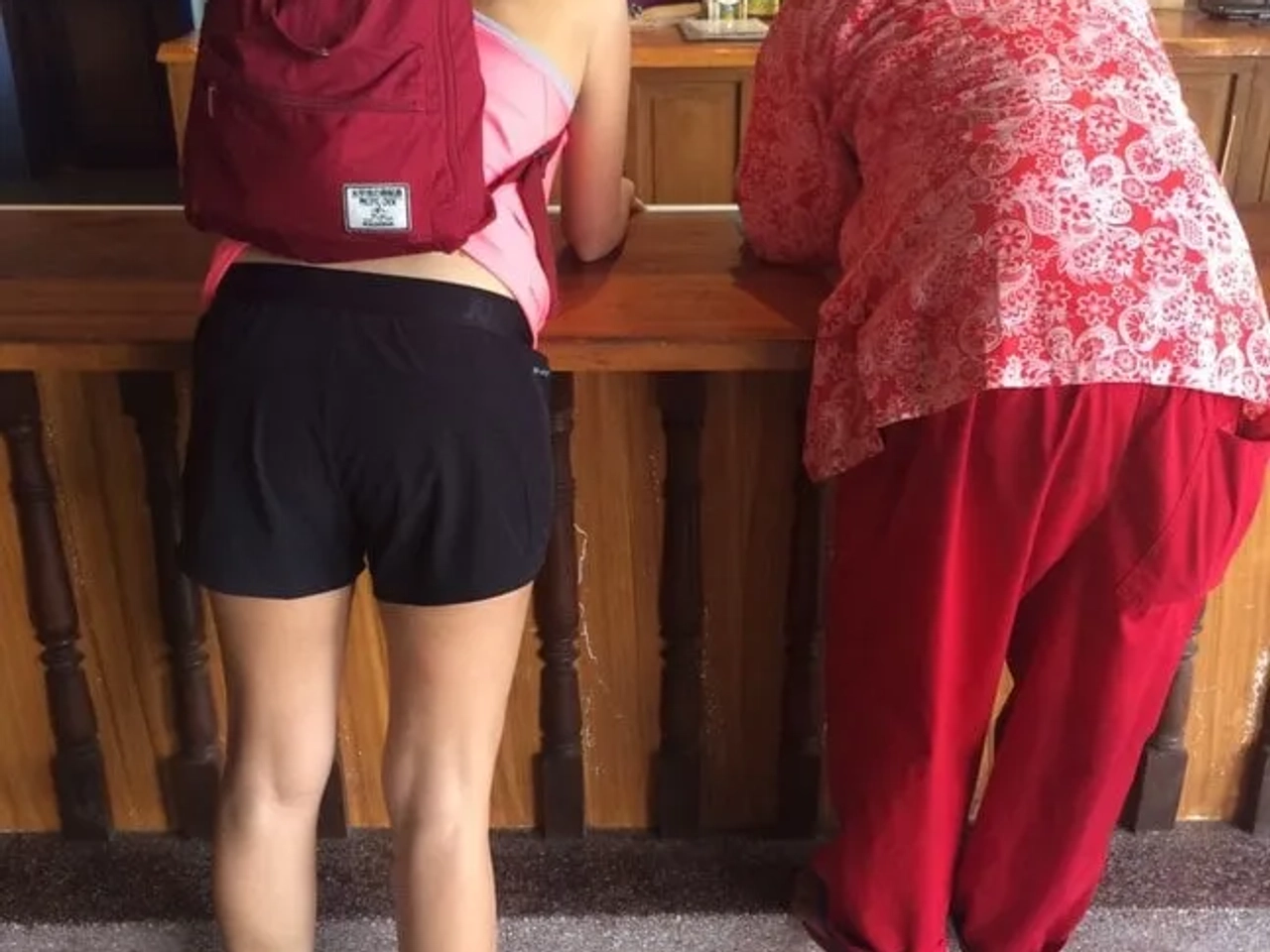 Dos personas de espaldas en un mostrador, una con mochila y otra en ropa colorida.