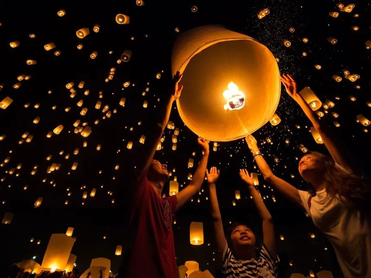 Familia lanzando linternas en un festival nocturno iluminado por luces flotantes.