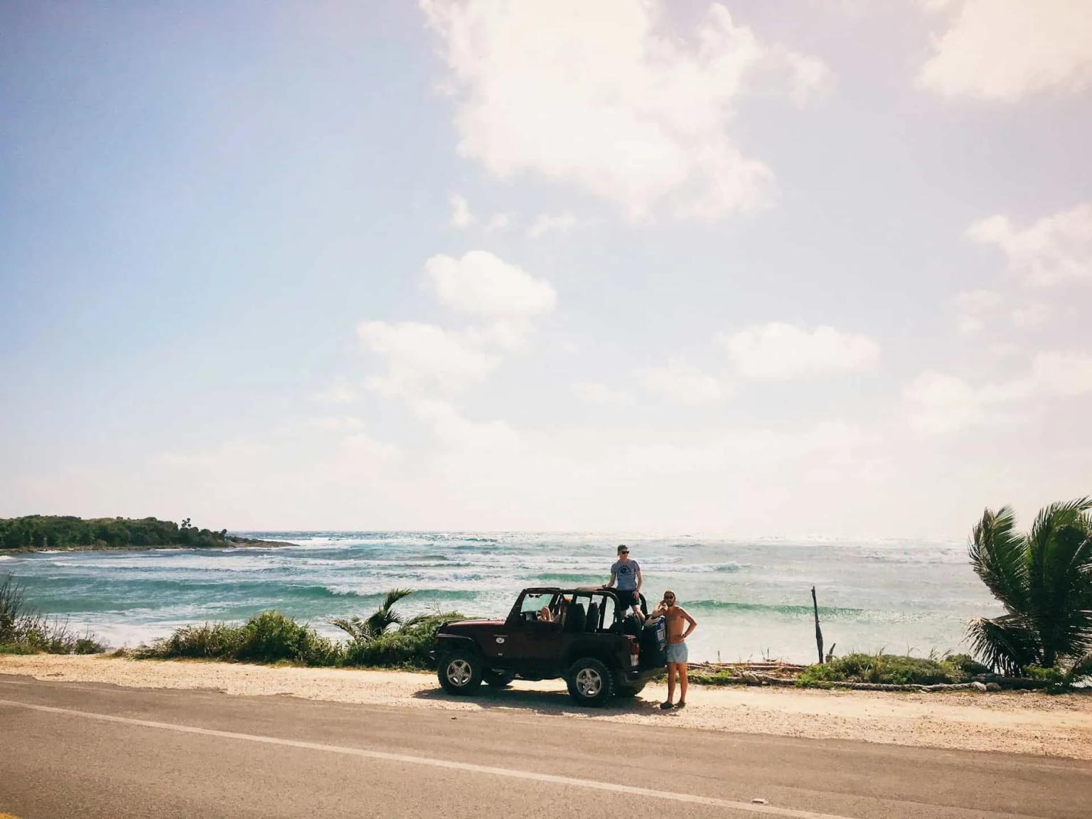 Grupo de pessoas ao lado de um carro em uma praia ensolarada.
