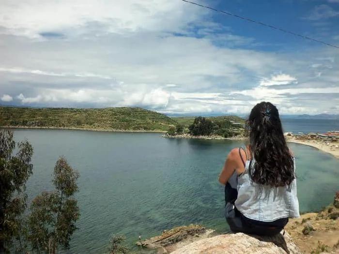 Mujer sentada contemplando un paisaje de lago y montañas.