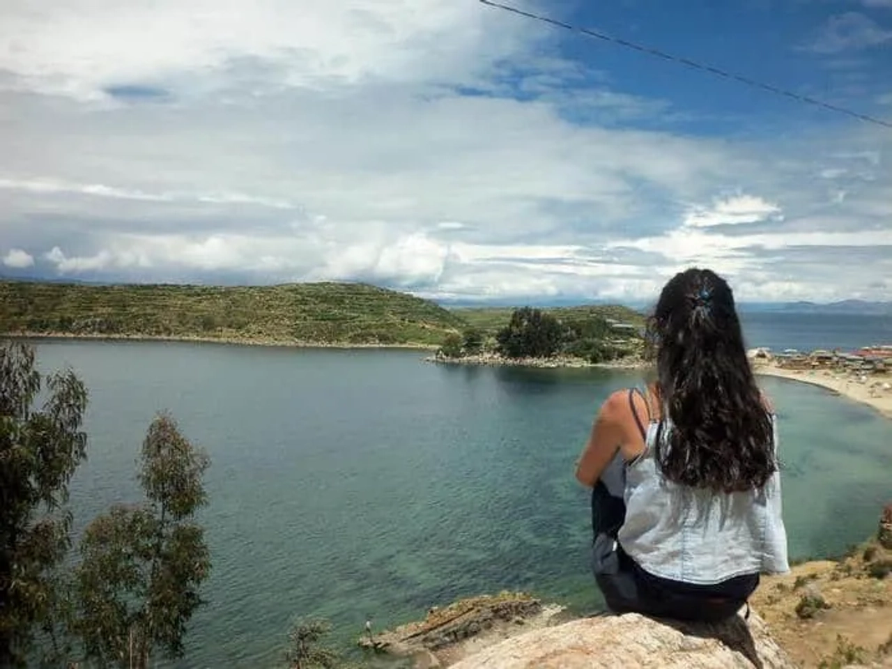 Mujer sentada contemplando un paisaje de lago y montañas.