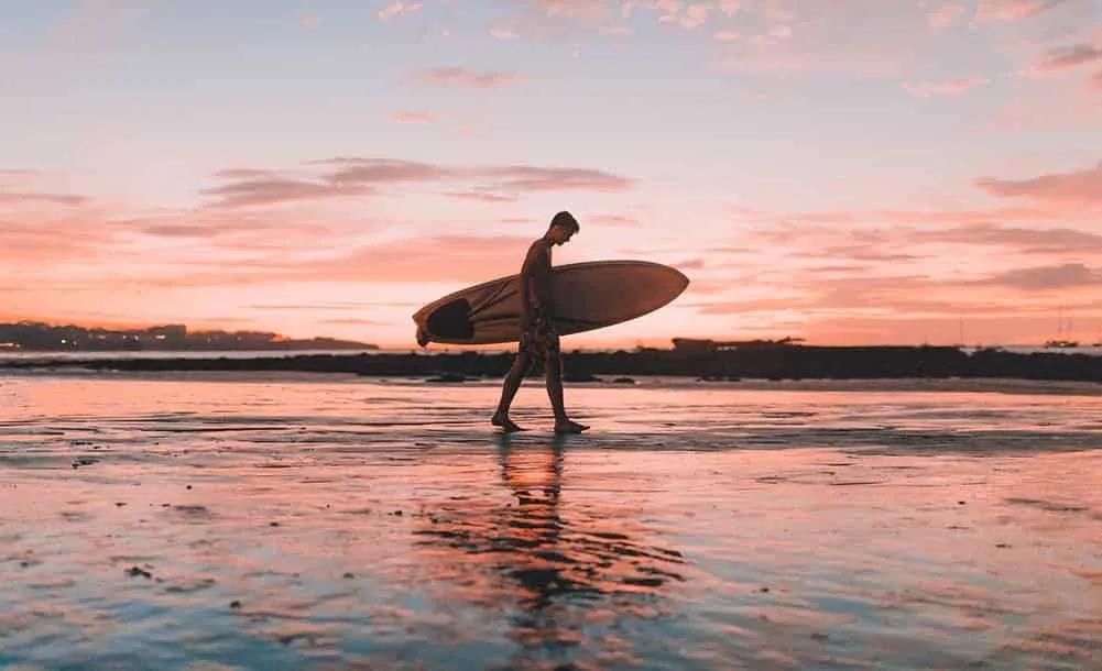 homem com prancha de surf na mão junto ao mar na costa rica
