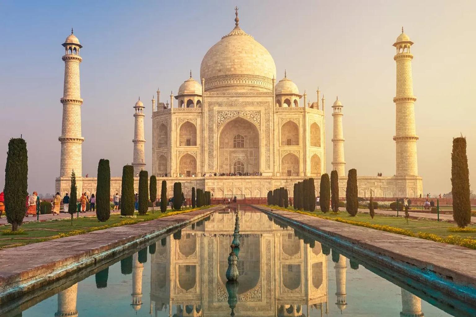 El Taj Mahal reflejado en un estanque, rodeado de jardines y torres.