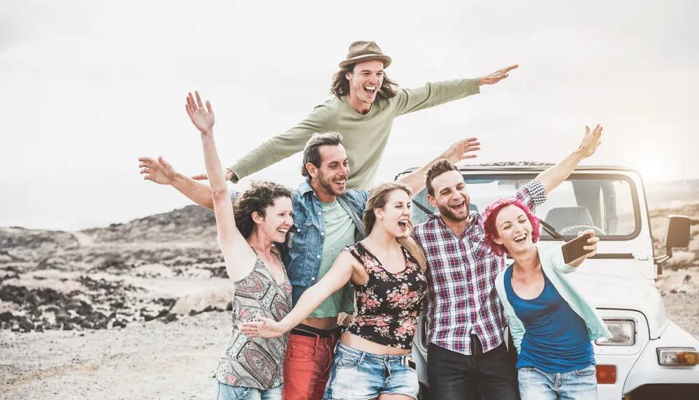 Grupo de amigos sorrindo e se divertindo ao ar livre, perto de um carro.