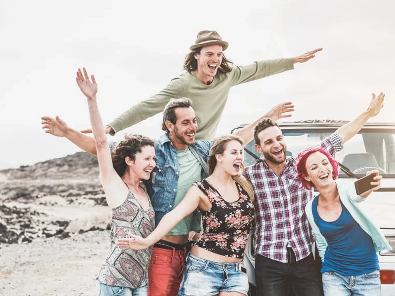 Grupo de amigos sorrindo e se divertindo ao ar livre, perto de um carro.