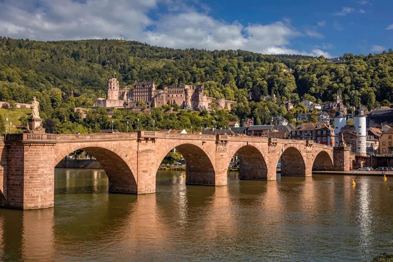 Ponte histórica sobre o rio, com castelo e montanhas ao fundo em Heidelberg.