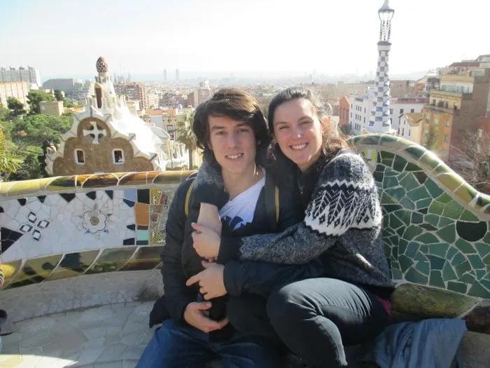Pareja sonriente en un parque con vista panorámica de la ciudad.