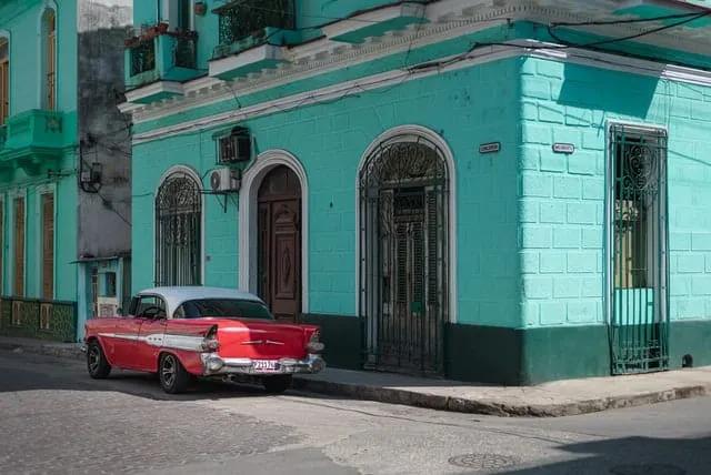 carro vermelho estacionado ao pé de prédio azul em Havana