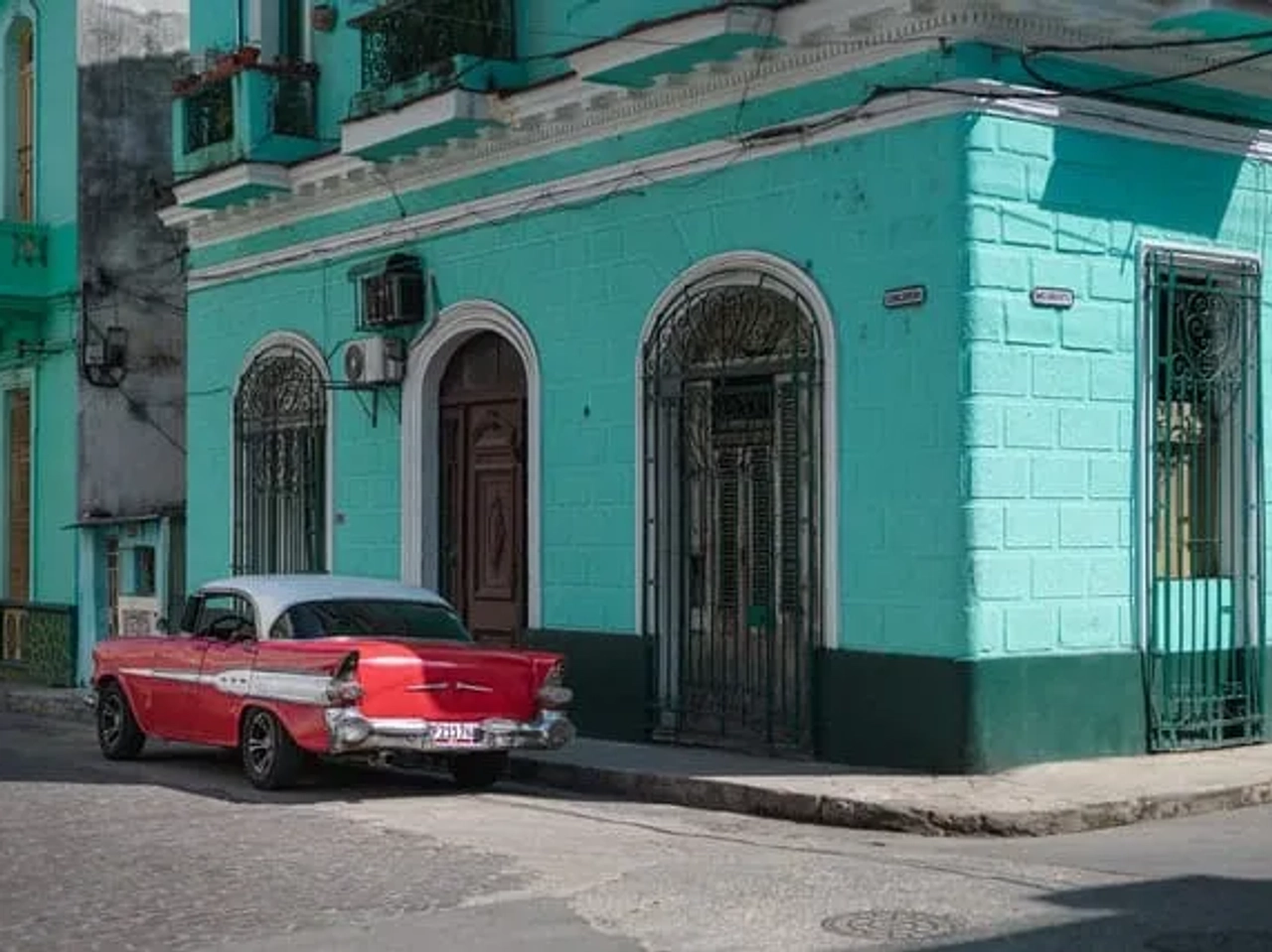 carro vermelho estacionado ao pé de prédio azul em Havana