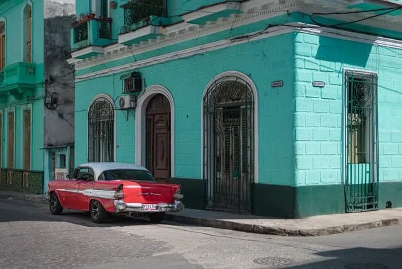 carro vermelho estacionado ao pé de prédio azul em Havana