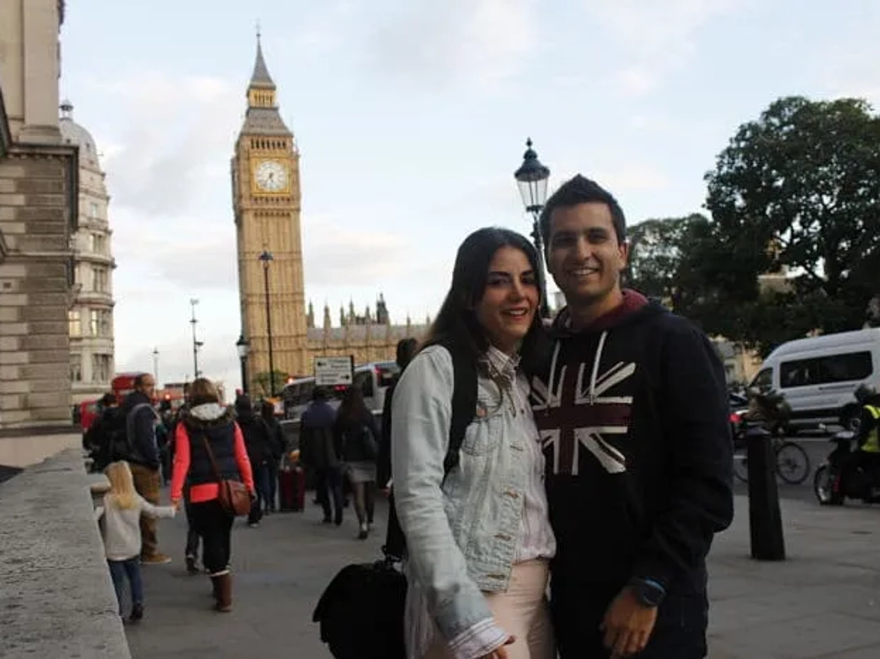 Pareja sonriente frente al Big Ben en Londres, rodeada de turistas.