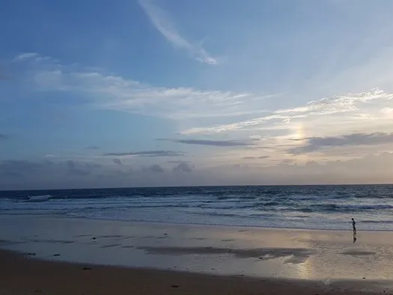 Playa tranquila al atardecer, con una persona caminando cerca del agua.