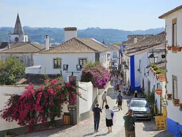 pessoas a passear em obidos num dia de sol junto às casas típicas da cidade