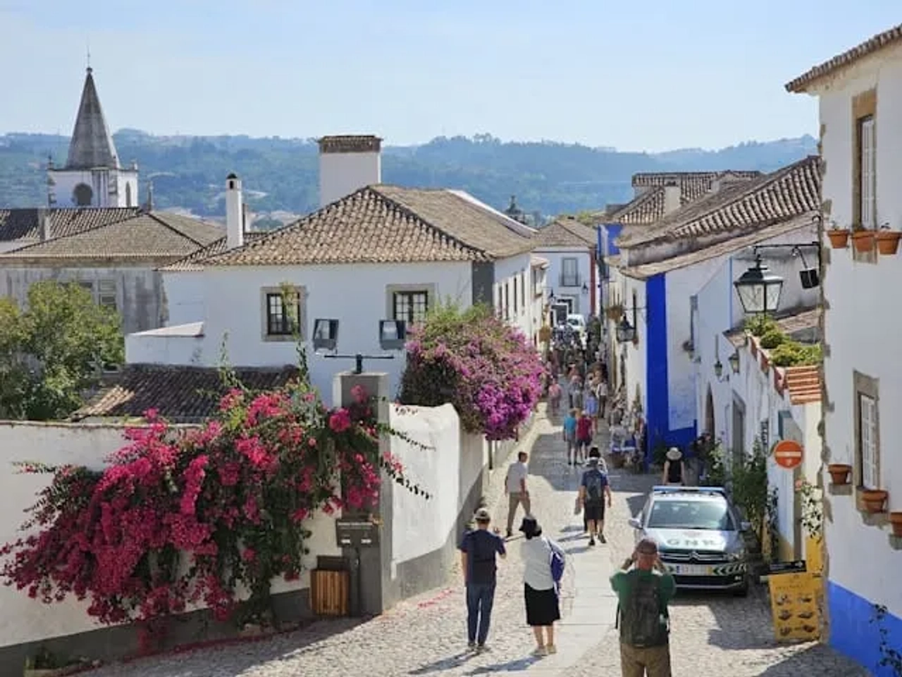 pessoas a passear em obidos num dia de sol junto às casas típicas da cidade