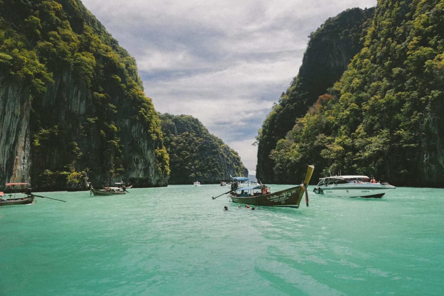 Cenário tropical com barcos em águas turquesa entre montanhas verdes na Tailândia.