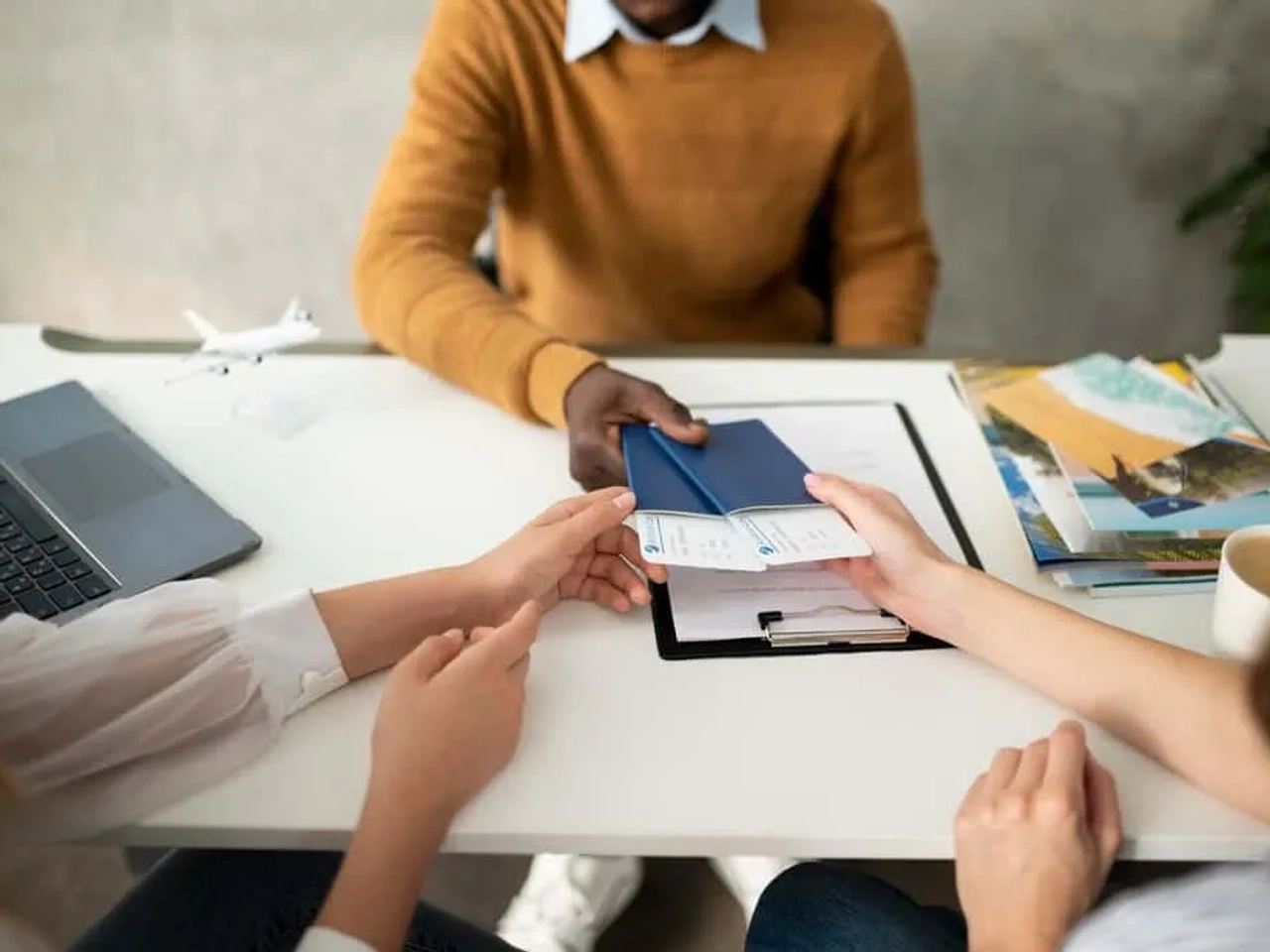 Pessoa entregando documentos de viagem a um agente em uma mesa de escritório.
