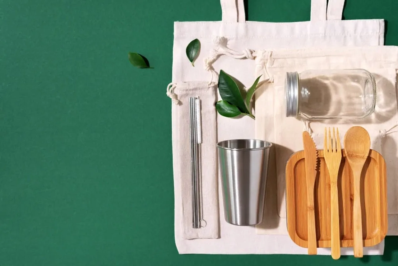 Conjunto de utensilios sostenibles: bolsa de tela, vaso de acero, jarra y cubiertos de bambú.