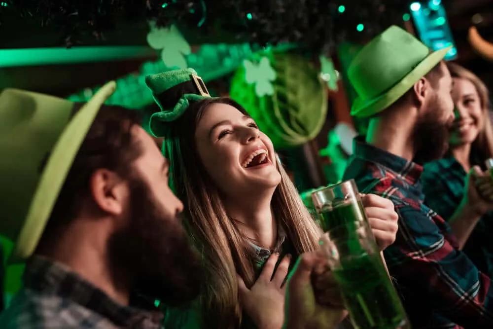 jovens com chapeus verdes riem e bebem cerveja