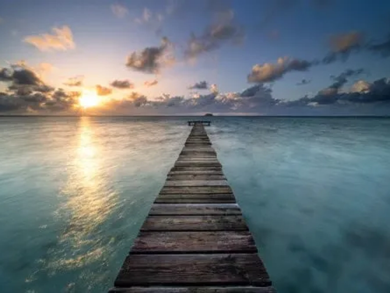 Muelle de madera sobre aguas tranquilas al atardecer en Polinesia Francesa.