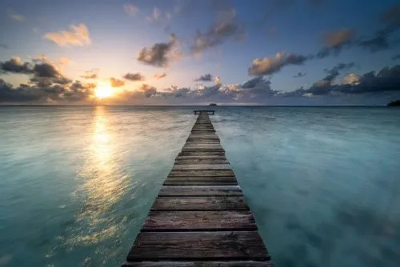 Muelle de madera sobre aguas tranquilas al atardecer en Polinesia Francesa.