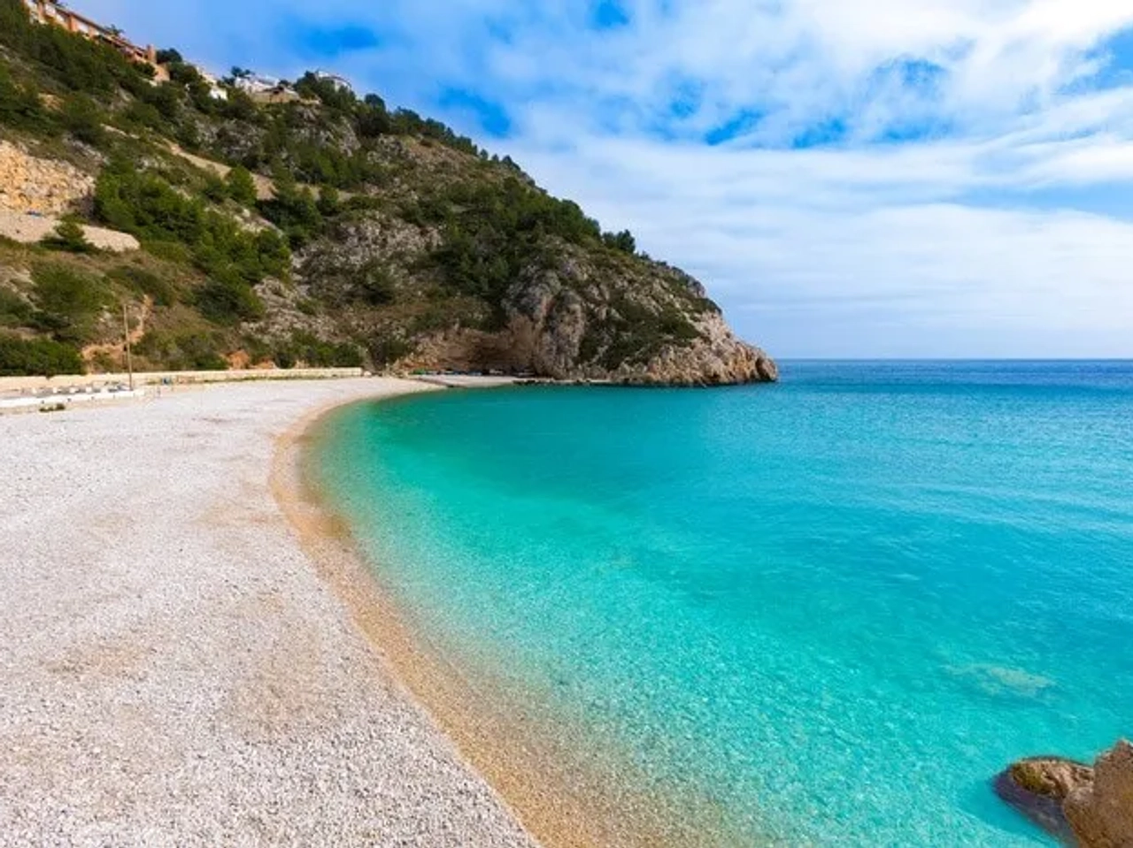 Playa de aguas turquesas y arena, rodeada de montañas y vegetación.
