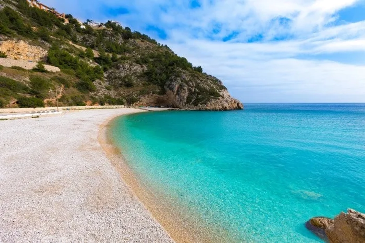 Playa de aguas turquesas y arena, rodeada de montañas y vegetación.